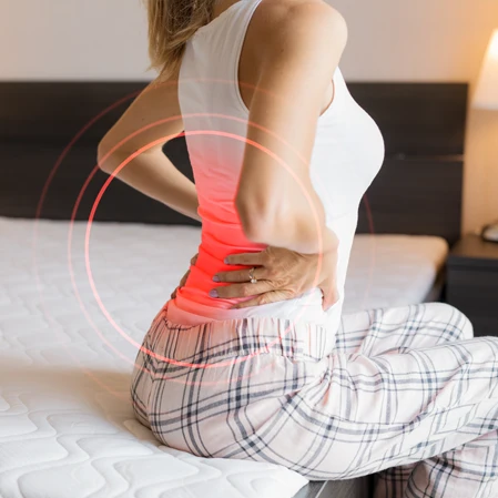 Person sitting on a bed with back pain.