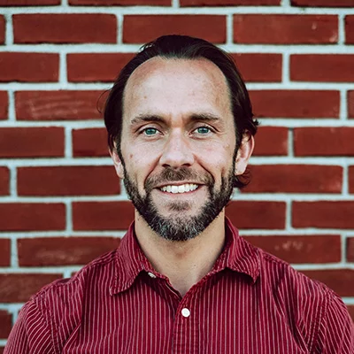 Dr. Pete Rom smiling in front of a brick wall.